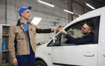 Young adult auto service specialist giving keys back to happy man after repairing his car, horizontal shot, copy space