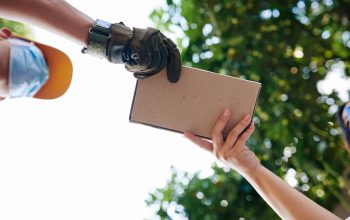 Delivery man in medical mask giving small cardboard box to customer, view from below