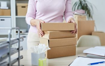 Stack of packed boxes with orders of online shop clients and manager taking one of them